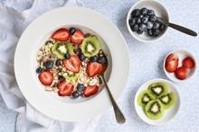 Bowl Of Muesli, Sliced Kiwifruit, Strawberries And Blueberries With A Spoon And Small Bowls Of Fruit.