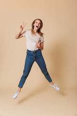 Poster - Full length portrait of excited blond woman 20s wearing casual clothing jumping and showing peace sign with two hands, isolated over beige background