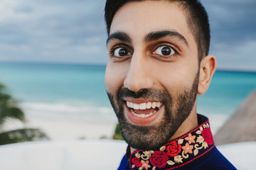 Wall Mural - Portrait of funny smiling Hindu groom standing before a seaside view