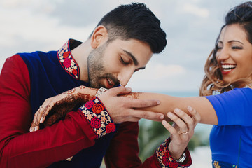 Groom holds tender hand of Hindu bride covered with henna tattoo