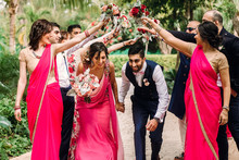 Bridesmaids Hold Their Bouquets Up While Bride And Pose In The Garden