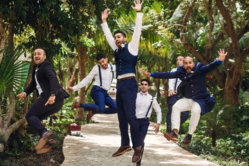 Wall Mural - Hindu groom and groomsmen have fun jumping outside in the garden