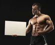 © Prostock-studio - Muscular bodybuilder holding white blank banner at black background