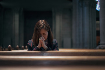 Wall Mural - A Christian girl is sitting and praying with broken heart in the church.