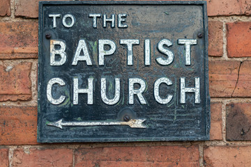 metal and enamel street sign on brick wall stating to the baptist church with arrow pointing to the 