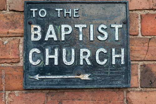 Fotografía metal and enamel street sign on brick wall stating to the baptist church with ar
