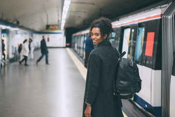 Happy young black woman inside the underground station waiting for the train