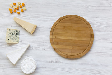 Set of various cheese with round bamboo board on a white wooden background. Copy space. From above, flat lay.