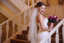 View From Behind Beautiful Blond Woman In Veil And Wedding Dress Holding Bouquet, Smiling And Climbing Up The Stairs Of The Big Hall.