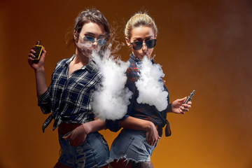 Wall Mural - Side view of trendy young female in glasses and shorts standing and smoking on studio background