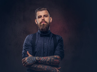 Wall Mural - Portrait of a handsome old-fashioned hipster in a blue shirt and suspenders, standing with crossed arms in a studio.