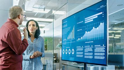 Canvas Print - Male and Female Business Workers in Conference Room Have Discussion about Statistics and Graphs Shown on a Presentation TV.