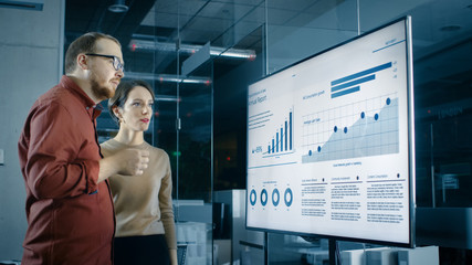 Poster - Male and Female Business Coworkers in Conference Room Have Discussion about Statistics and Graphs Shown on a Presentation TV.