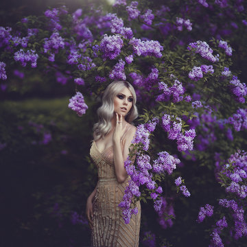 Spring style. Beautiful sensual girl blonde in spring. Blossoming spring garden. Young girl in a gold elegant dress. young woman in the garden with blooming purple bushes