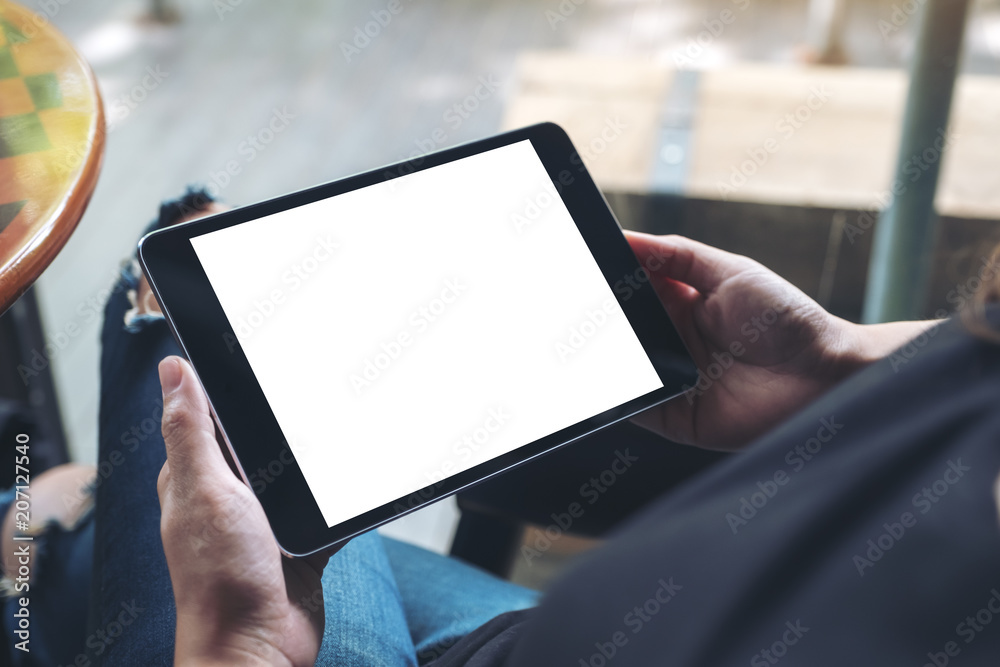 Mockup image of a woman sitting cross legged and holding black tablet pc with blank white desktop screen - obrazy, fototapety, plakaty 