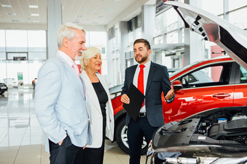 Aged couple look  new car with dealer in car showroom.