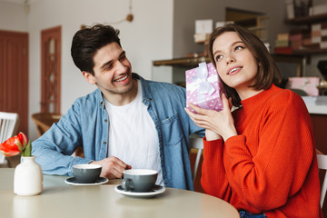 Poster - Excited young couple sitting at the cafe table