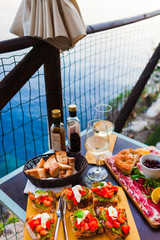 Wall Mural - Romantic dinner for two at sunset. White wine and Tasty italian snack: fresh bruschettes  and meat on the board in outdoor cafe with amazing view in Manarola