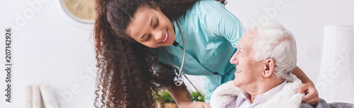 Fotomural Panorama of a happy nurse with a stethoscope covering an elderly man with a blan
