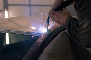 Wall Mural - Experienced man performs work on body repair car with a welding machine. Repair of the roof of the vehicle.