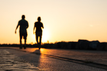 Silhouette Of Young Couple Runner Are Running In Park At Evening Sunset.