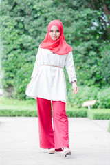 Wall Mural - Portrait of happy young muslim woman red hijab Standing poses over blurred the green field background.