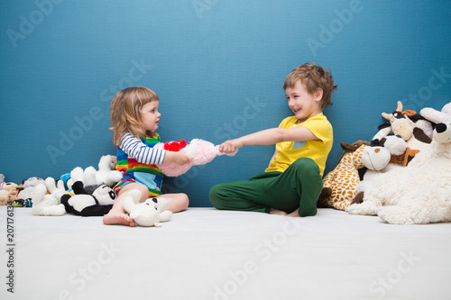 Two little kids, brother and sister fighting over a toy Fototapeta