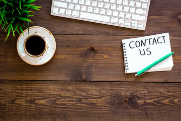 Poster - Template for contacts, background for contact information. Lettering Contact us in notebook on office work desk with computer on dark wooden background top view space for text