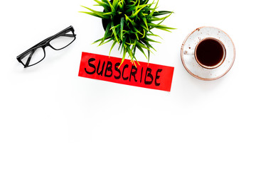 Poster - Email subscribe concept. Hand lettering subcribe on work desk with plant, glasses, cup of coffee on white background top view copy space