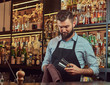 © Fxquadro - Stylish brutal barman is cleaning the glass with a cloth at bar counter background.