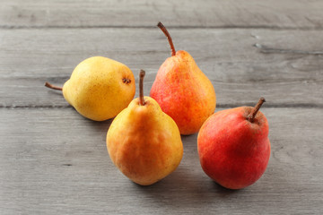 Four ripe red and yellow pears on gray wood desk.