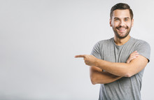 Look Over There! Happy Young Handsome Man In Jeans Shirt Pointing Away And Smiling While Standing Against White Background