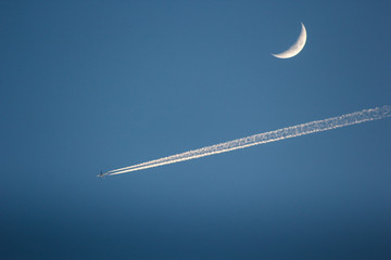 jet plane flying past a half moon on blue sky