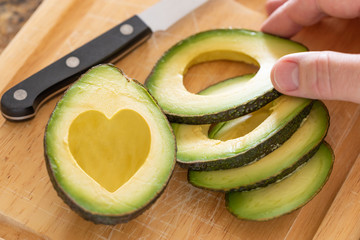 Male Hand Prepares Fresh Cut Avocado With Heart Shaped Pit Area On Wooden Cutting Board