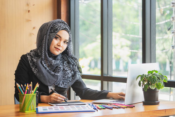Leinwandbilder - Young muslim asian female designer using graphics tablet while working with computer at studio or office.	