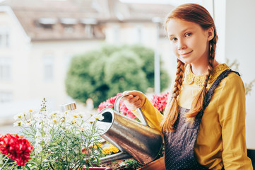 Adorable little girl watering plants on the balcony on a nice sunny day