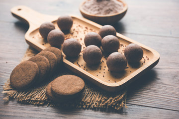 Nachni / Ragi laddu and biscuits or cookies made using  finger millet, sugar and ghee. It's a healthy food from India. Served in a bowl or plate with raw whole and powder. Selective focus