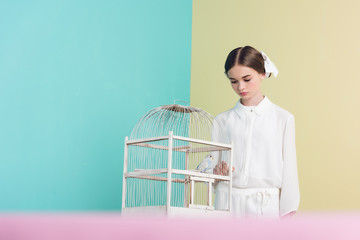 attractive fashionable girl with parrot in white cage