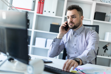 Wall Mural - A young man is sitting in the office, talking on the phone and working on the computer.