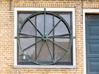 Wall Mural - Window with round wheel of steel, part of facade of house in old town of Makkum, Friesland, Netherlands