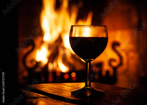 Fotografía Glass of red wine on the wooden table with burning fire on the background