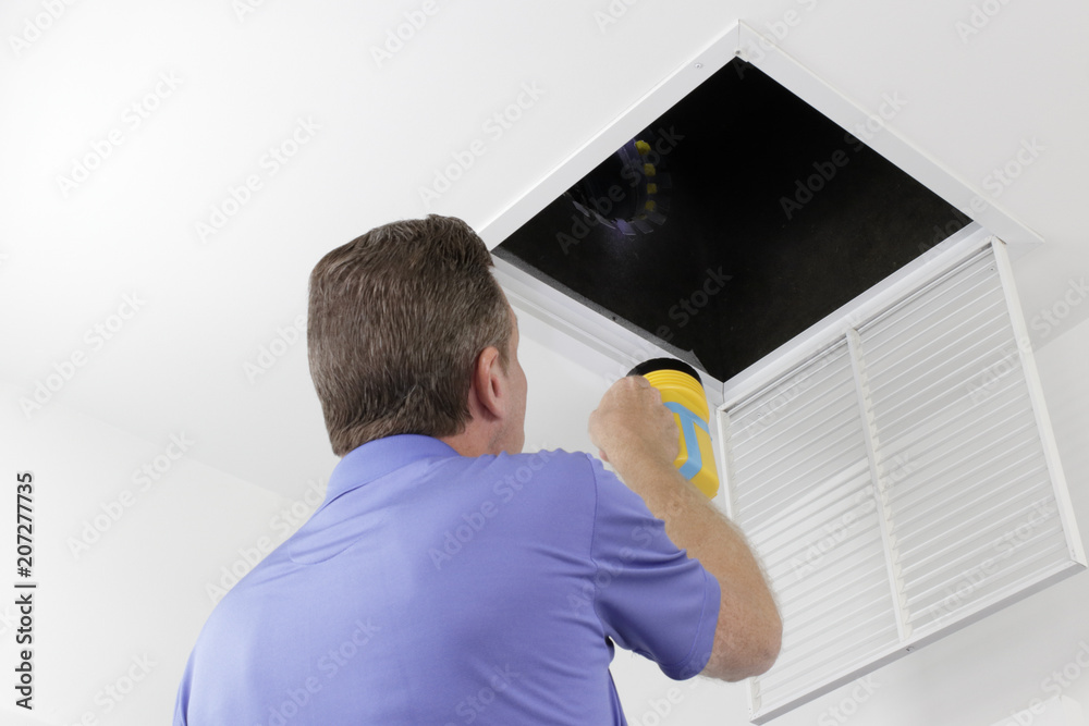 Man Inspecting an Air Duct with a Flashlight.Older male with a yellow flashlight examining HVAC ducts in a large square vent. Male technician looking over the air ducts inside a home air intake vent. - obrazy, fototapety, plakaty 