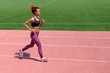 © romsvetnik - An African American in the summer sports. A young sexy sporty black girl runs along the pink path of the stadium next to the green grass.