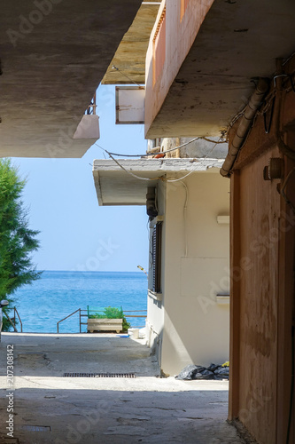 Fotografia  A narrow alley leading out to the turquoise sea. Crete, Greece.