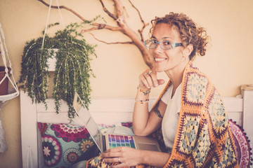 nice beautiful middle age caucasian woman sit down with a cover on the shoulder for the spring cold working on the terrace with a colored laptop. smile and happy to work at home in alternative way