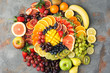 © Liliya Trott - Healthy fruits background in rainbow colours oranges apples grapes pears mango strawberries kiwis on the grey concrete table, top view, copy space, selective focus
