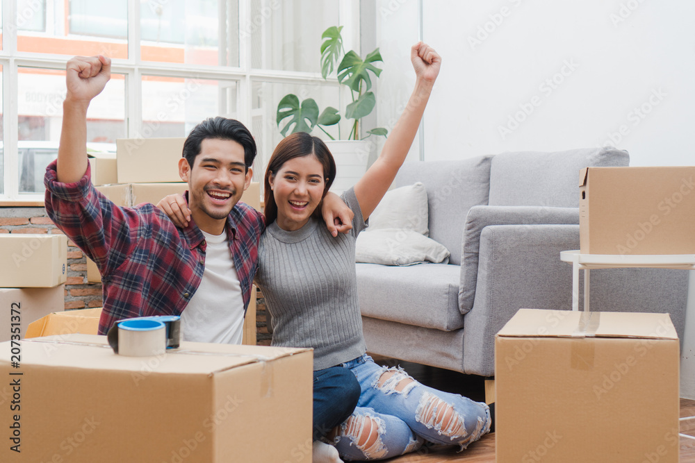 new house / home moving and relocation concept. Happy asian new married couple looking at each other face after moving in new apartment and start new life together. - obrazy, fototapety, plakaty 