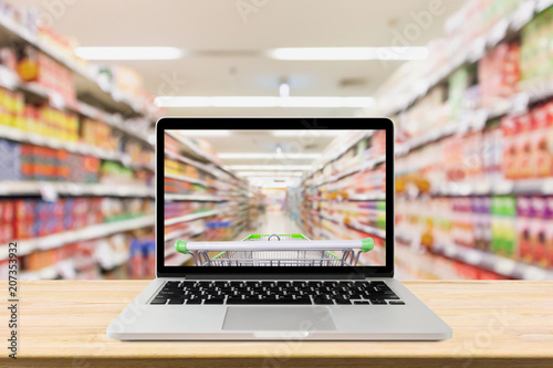 Fotografía laptop computer on wood table with supermarket aisle blurred background online s