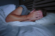 © TheVisualsYouNeed - restless worried young attractive man awake at night lying on bed sleepless covering face with hands suffering problem or insomnia sleeping disorder depressed