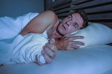 Portrait Of Young Attractive Scared Man In Fear And Panic Suffering Horror Nightmare Covering Face With Blanket Sleepless At Night Lying On Bed